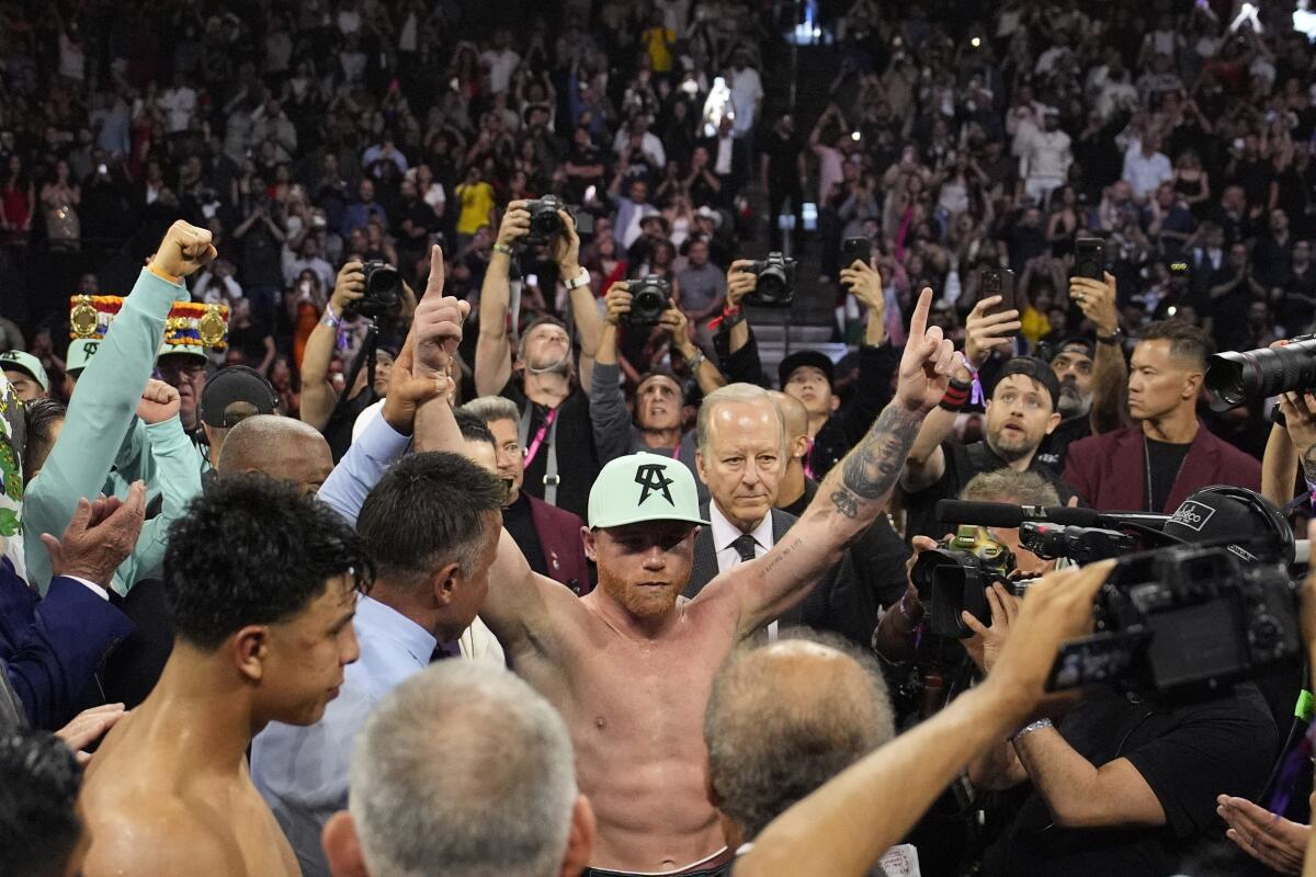 Canelo lvarez raises his arms and celebrates after defeating Jaime Munguia during a super middleweight title fight 