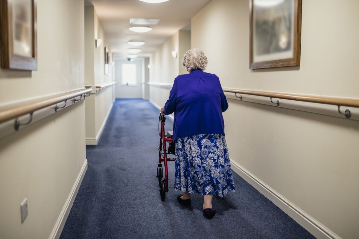 A senior woman walking down a corridor with the assistance of a walker. view from rear