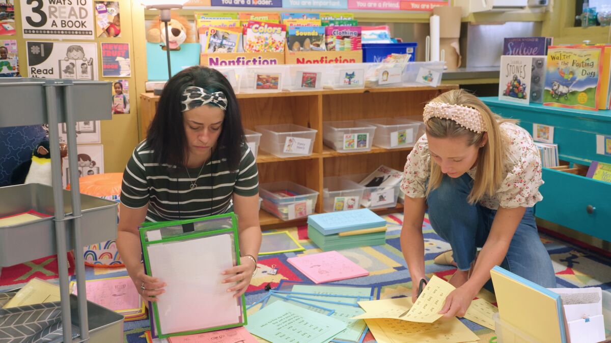 A teacher prepares for her class with the help of an assistant.