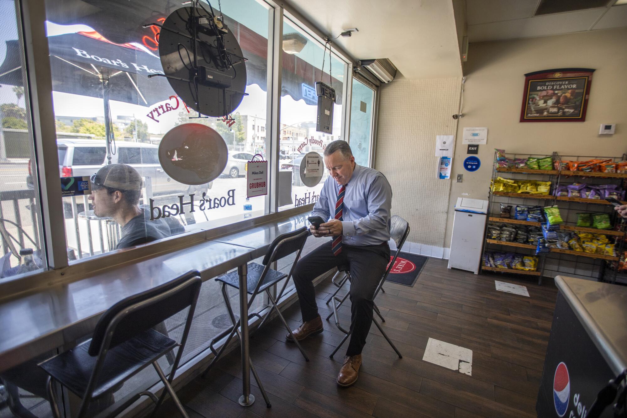 L.A. County Sheriff Alex Villanueva seated on a folding chair near a deli counter and snacks