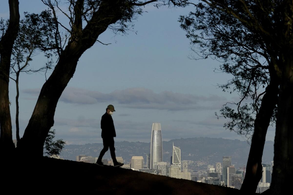 A person wearing a face mask walks atop Tank Hill in front of the skyline during the coronavirus pandemic in San Francisco.  
