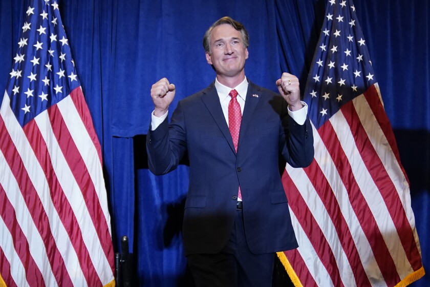 Glenn Youngkin holds up his fists while standing between two U.S. flags.