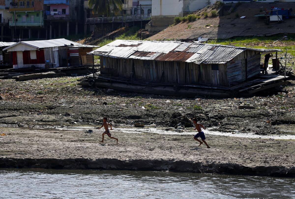 Un par de niños corren junto a una casa flotante varada en lo que solía ser la ribera del río Negro, en medio de una sequía en Manaos, Brasil, el martes 26 de septiembre de 2023. (AP Foto/Edmar Barros)