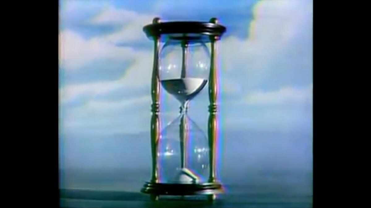 A video still shows an hour glass against a sky blue background