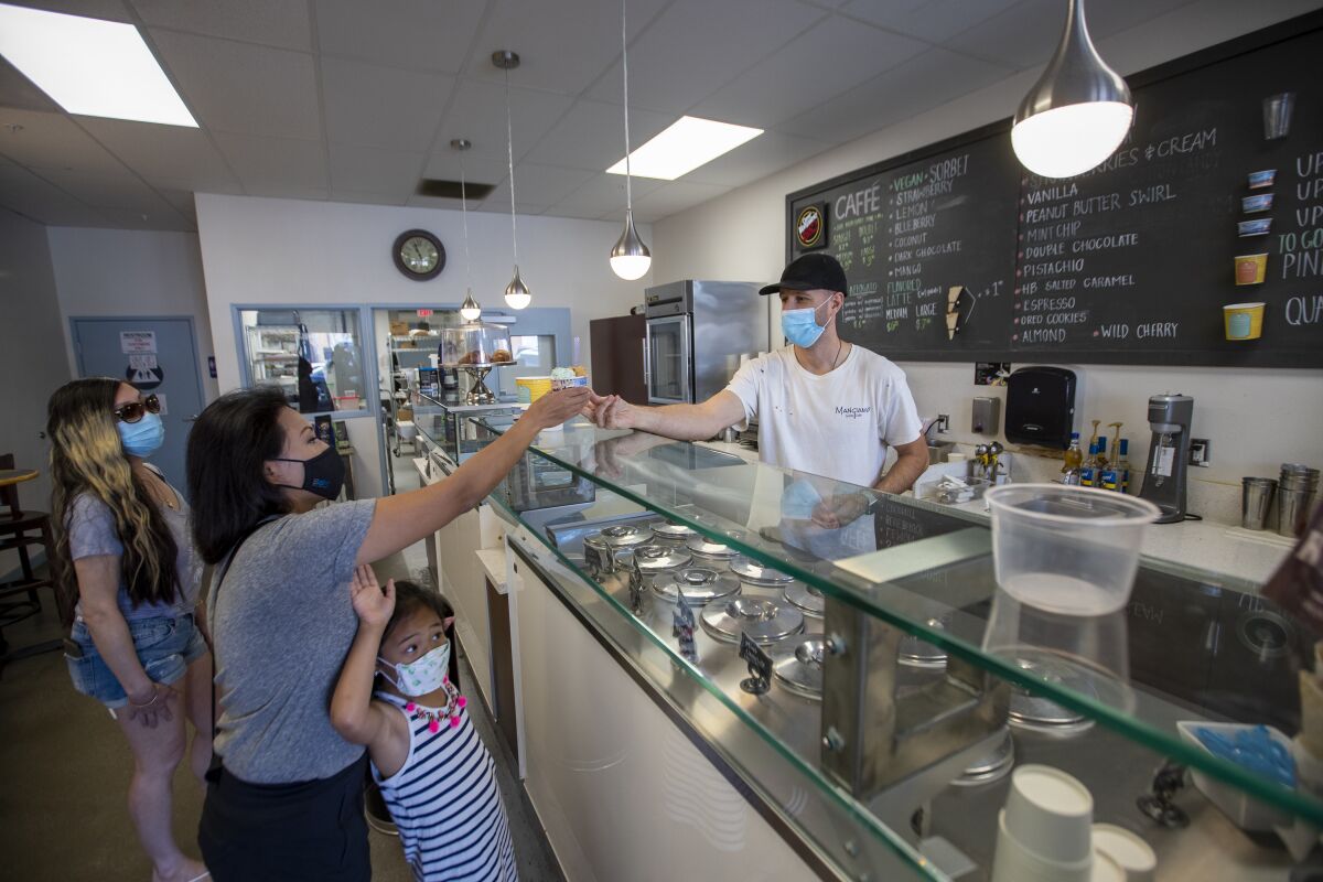 A shopkeeper in a mask hands gelato to customers over the counter