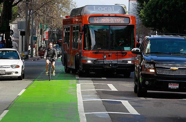 Crews work on the television show "Ringer" as bicyclists, cars and buses pass in the neon green bike lane in the 400 block of Spring Street in Los Angeles. The lane has been criticized by the film industry, which frequently uses the street as a stand-in for other cities and eras.