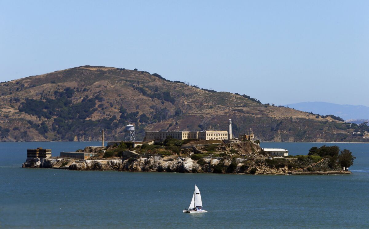 A sailboat passes Alcatraz on a sunny day in San Francisco.