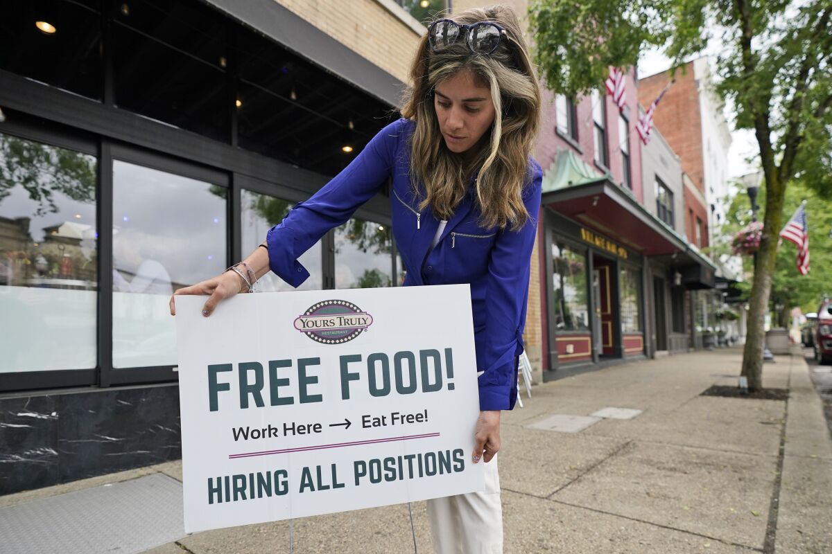 A woman puts out a sign that says, "Free Food! Work here - eat free. Hiring all positions"