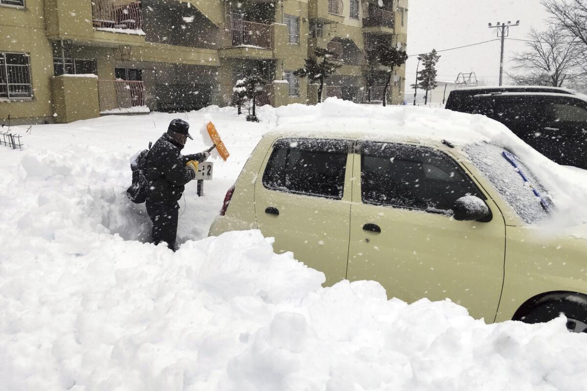 A man surrounded by waist-high snow works to dig out a car.