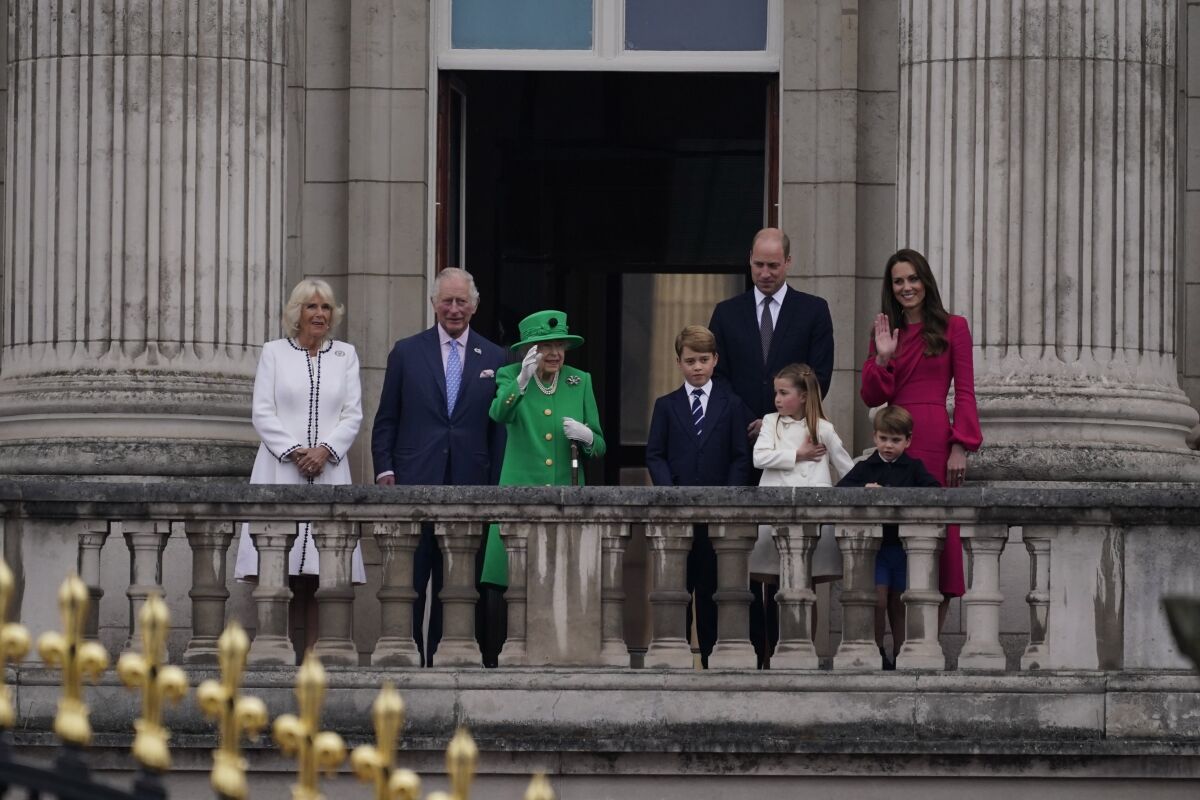 Queen Elizabeth II waves from a balcony with her family.