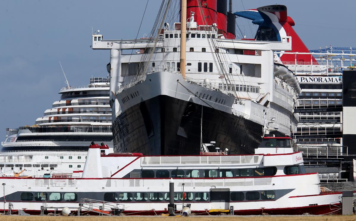 The Queen Mary is berthed between tour boats and a cruise ship in the Port of Long Beach.