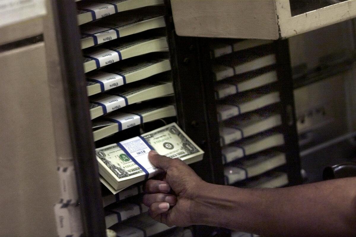 A hand pulls a bundle from a stack of $1 bills 