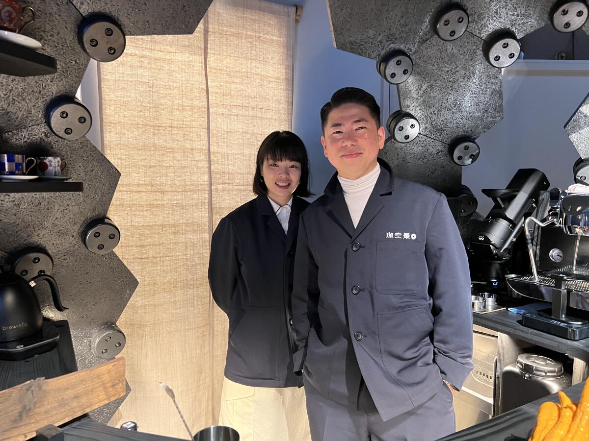 A Japanese woman and man stand inside the opening of a large black orb.