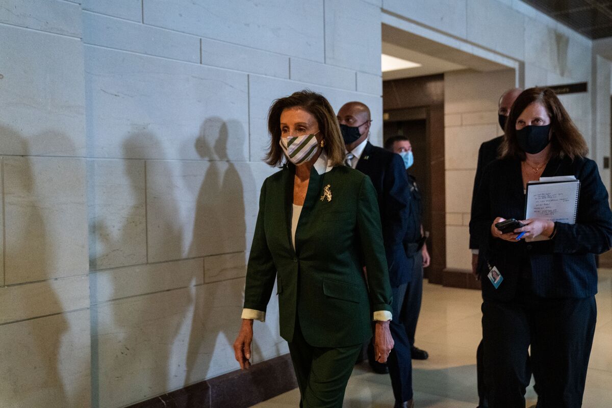 Two masked women in dark pantsuits walk in front of masked men in suits 