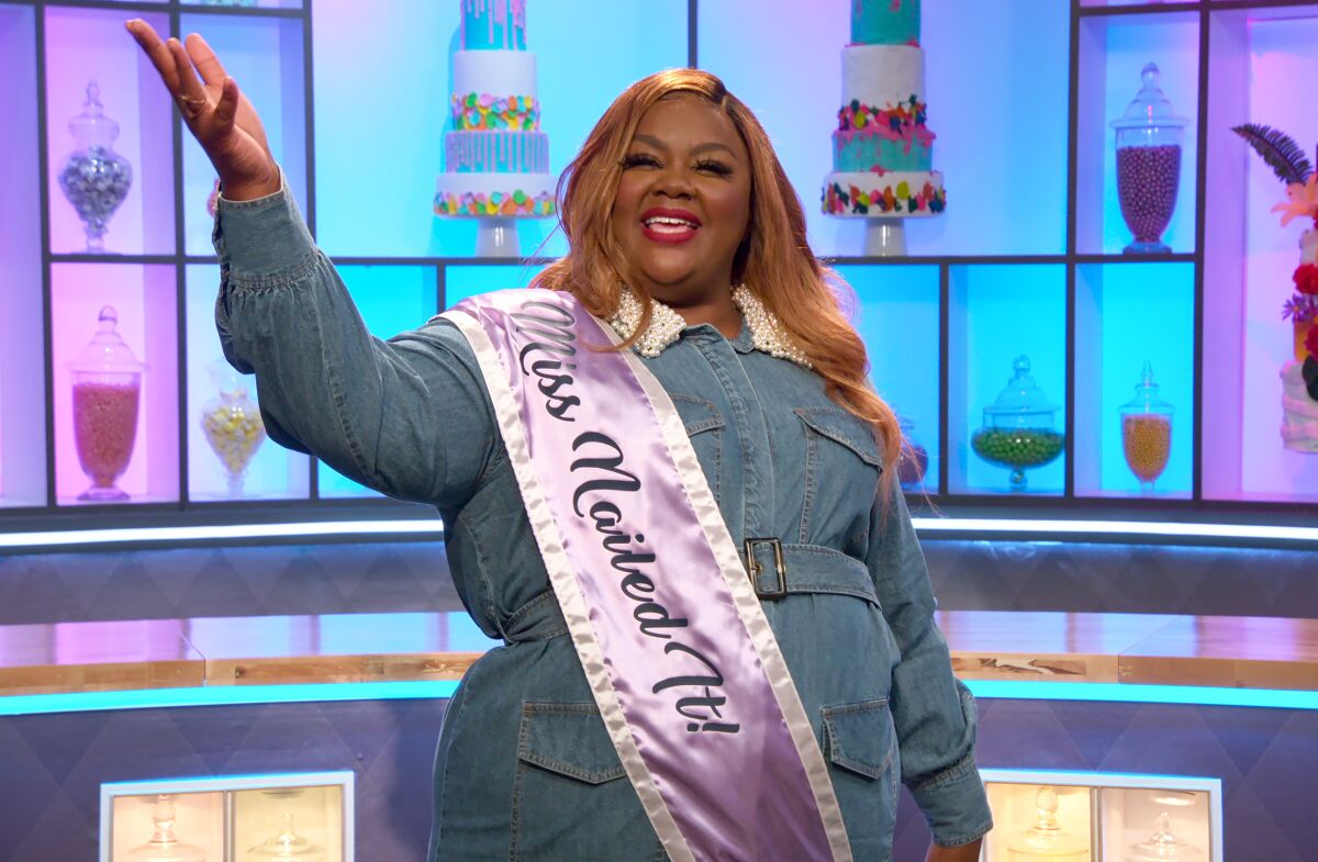 Host Nicole Byer, wearing a "Miss Nailed It!" sash, greets the crowd in an episode of "Nailed It!"  