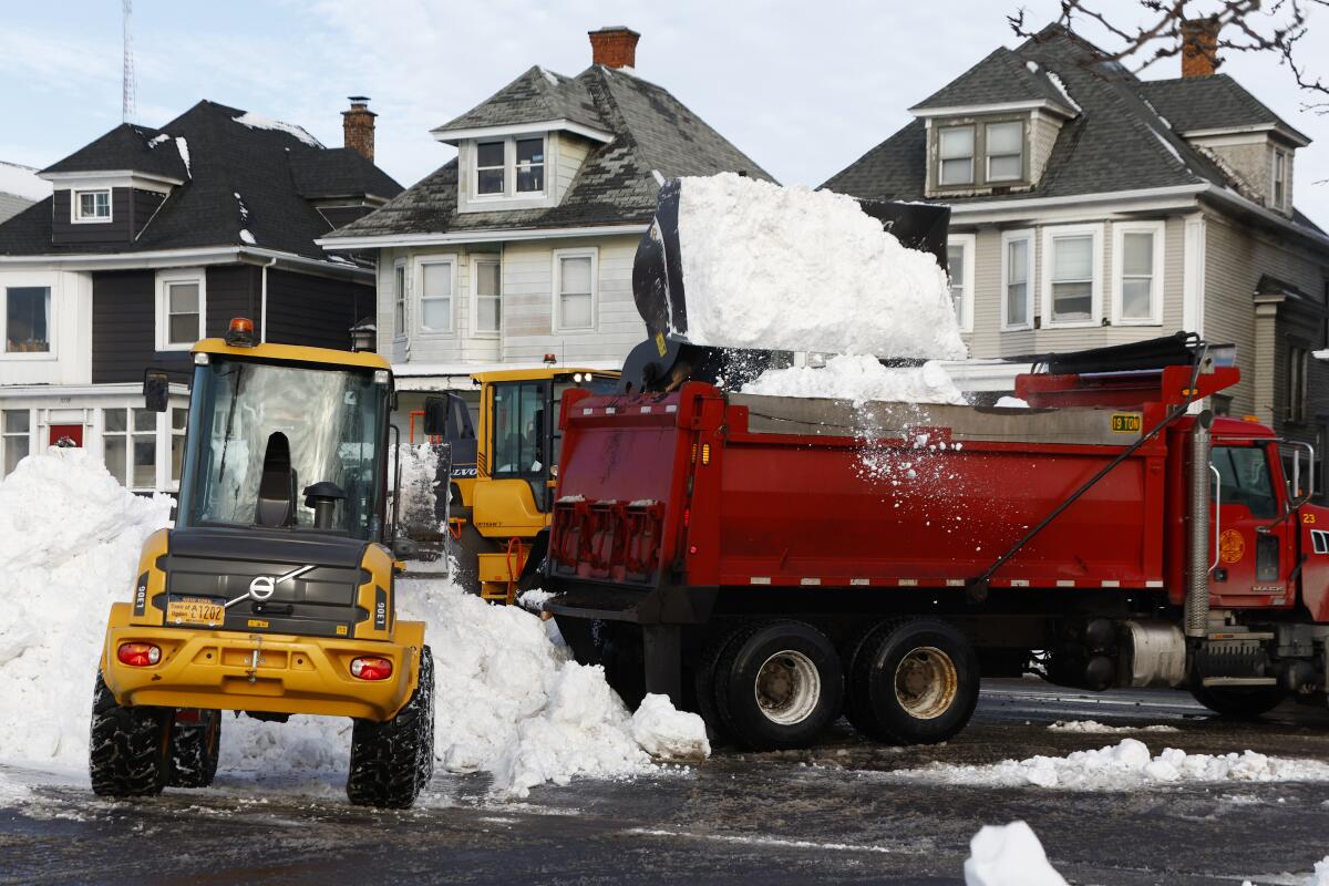 A front-end loader dumps snow into a dump truck.