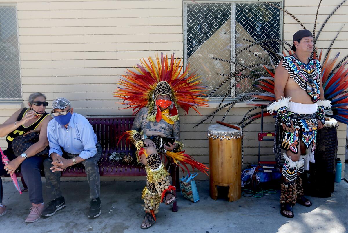 March participants, including two dancers in traditional Aztec garb, rest in the shade on a bench at Ruben Salazar Park