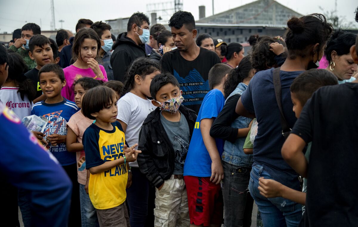 Adults and children wait in a thick line outdoors.
