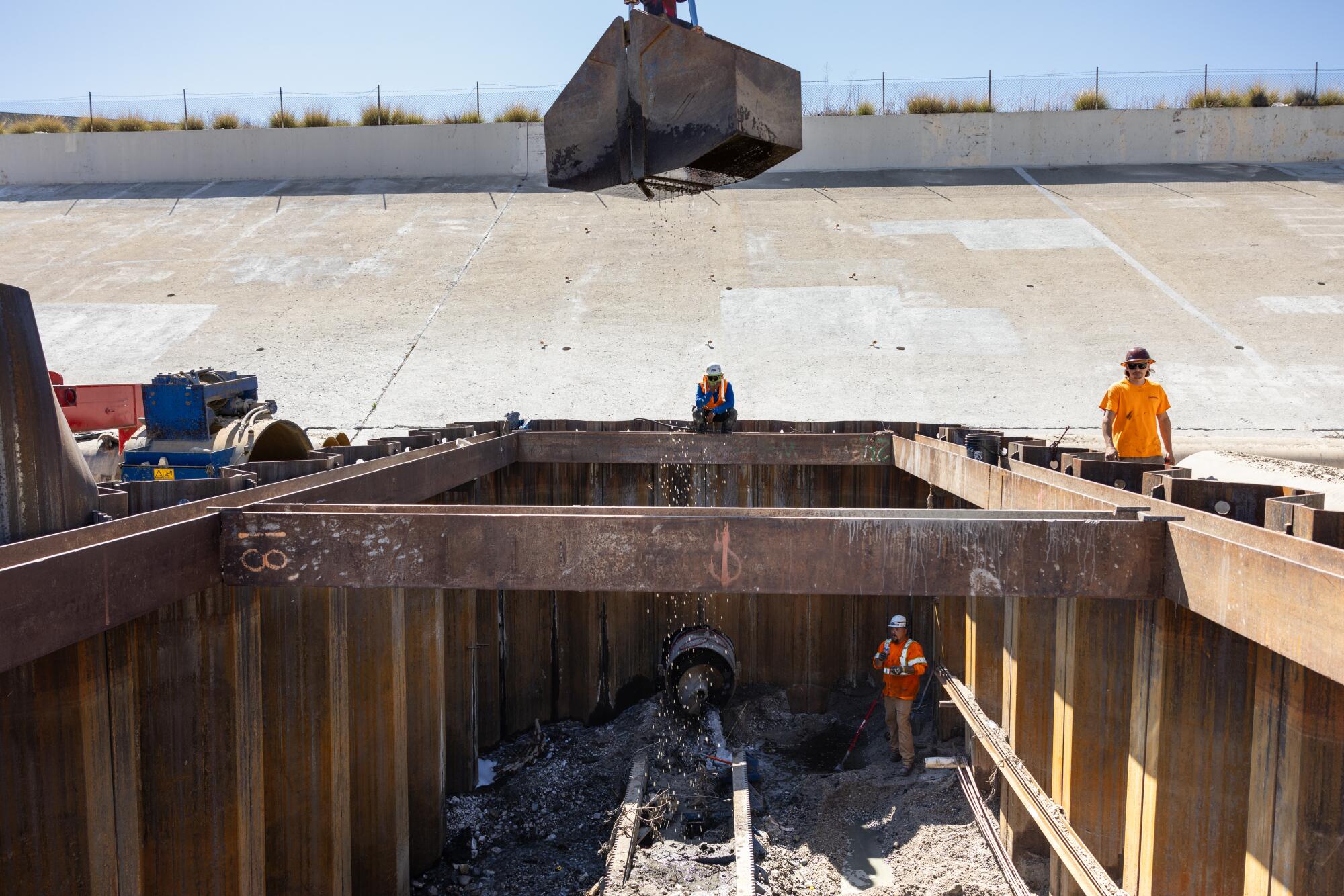 Construction workers in safety vests look over a dig pit in the concrete bed of the L.A. River.