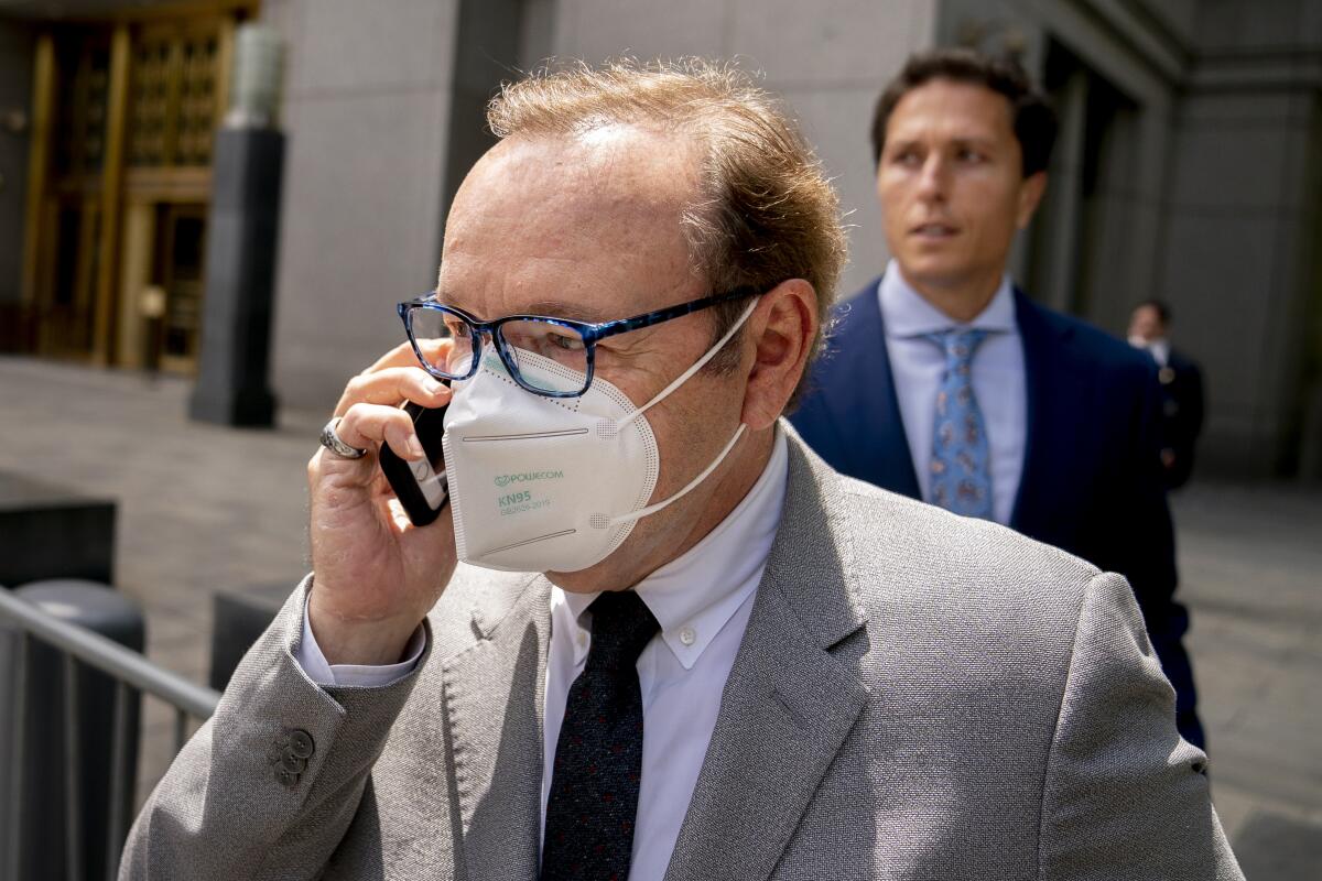 A man wearing eyeglasses and a face mask talks holds a cellphone while leaving a courthouse
