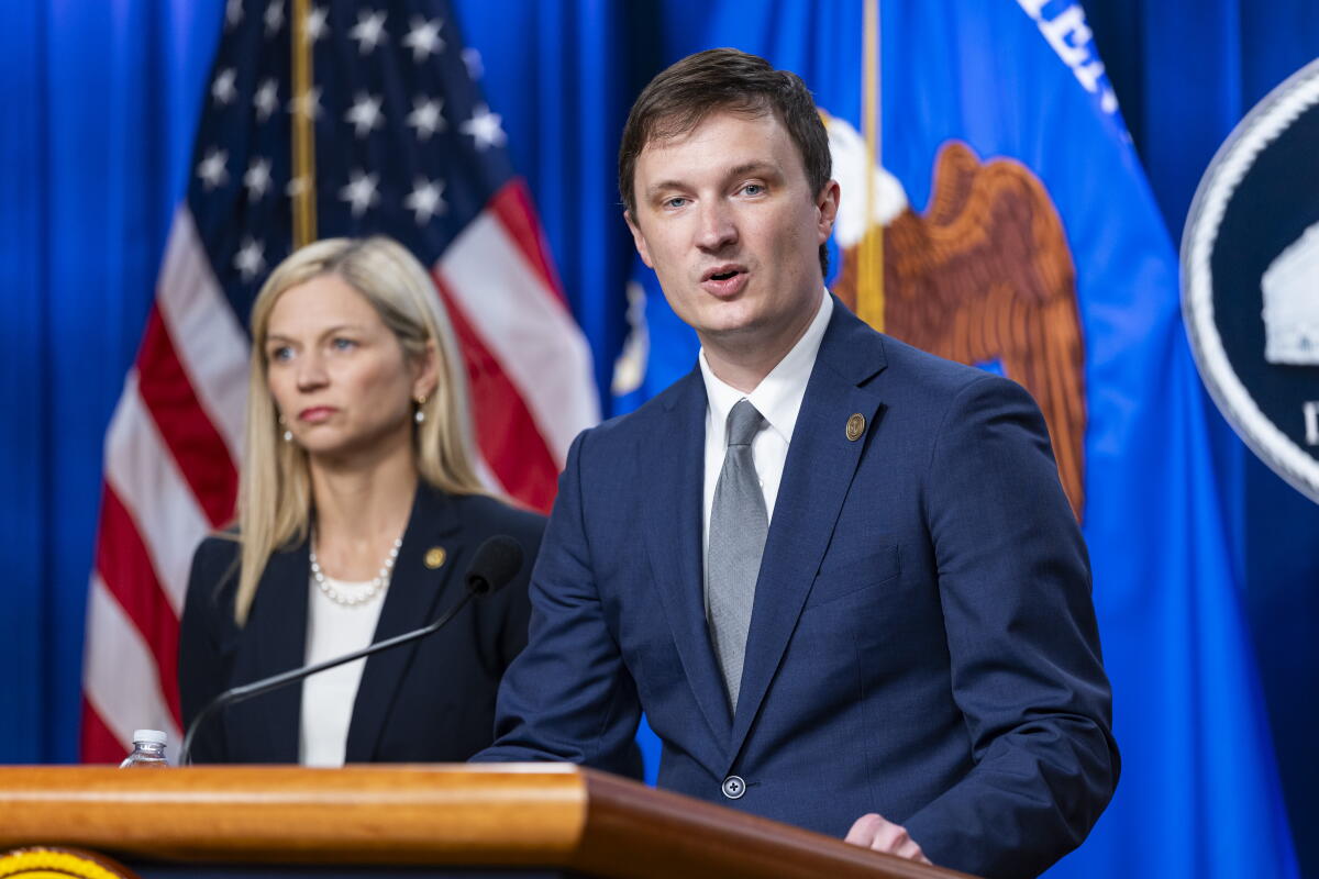 A man and a woman stand at a lectern while the U.S. flag is in the background