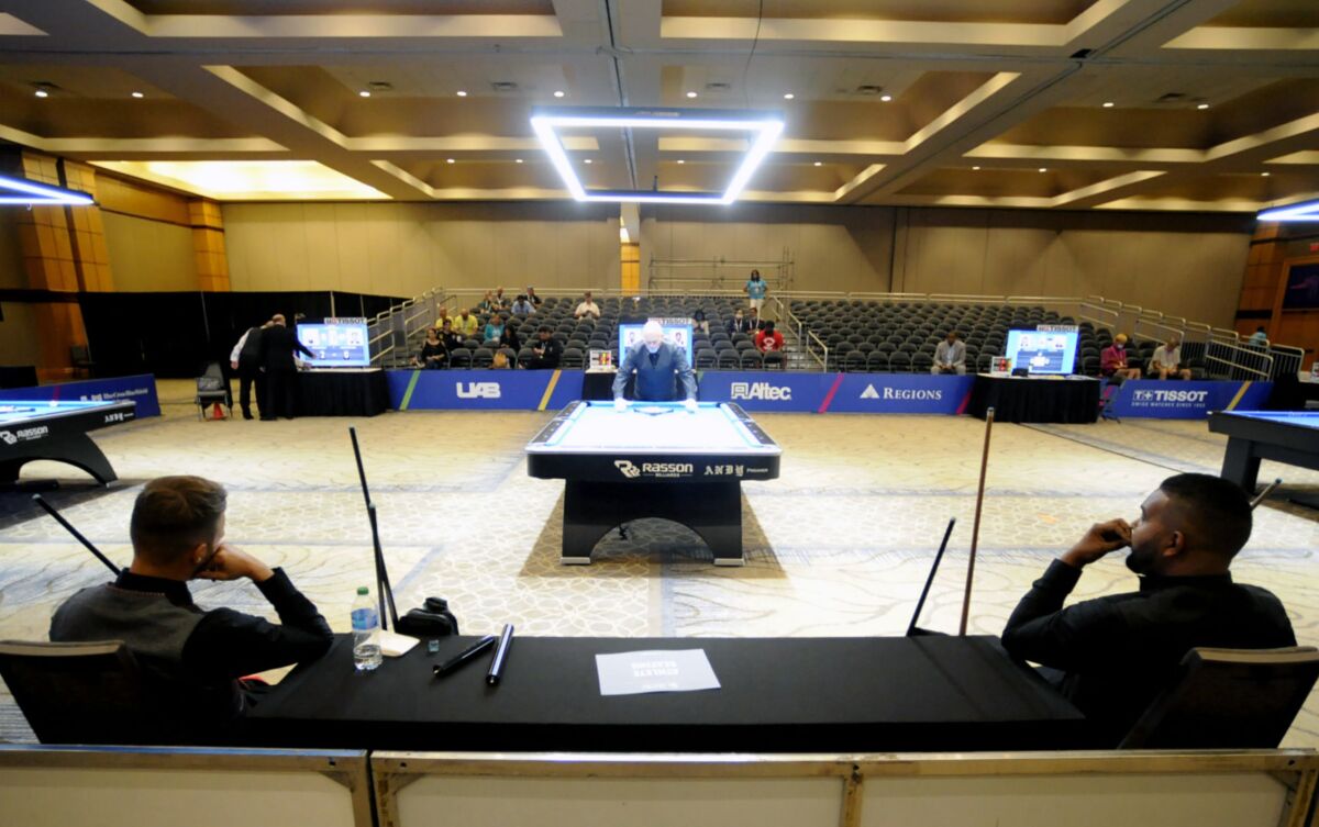 Austrian billiards players Albin Ouschan, left, and Aden Carl Joseph of South Africa sit on opposite ends of a table as a referee prepares the table for competition at The World Games in Birmingham, Ala., on Wednesday, July 13, 2022. (AP Photo/Jay Reeves)