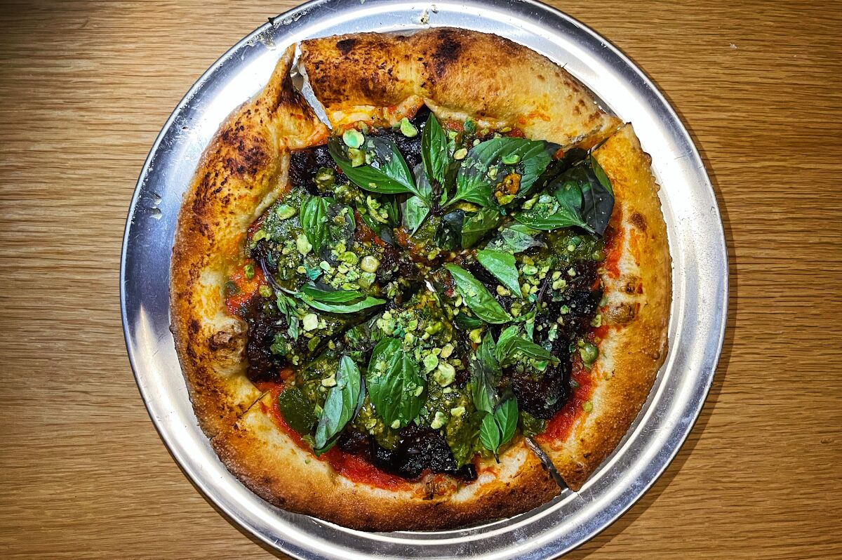 An overhead photo of a personal pizza covered in toppings of Thai basil, black bean mole and wasabi peas.
