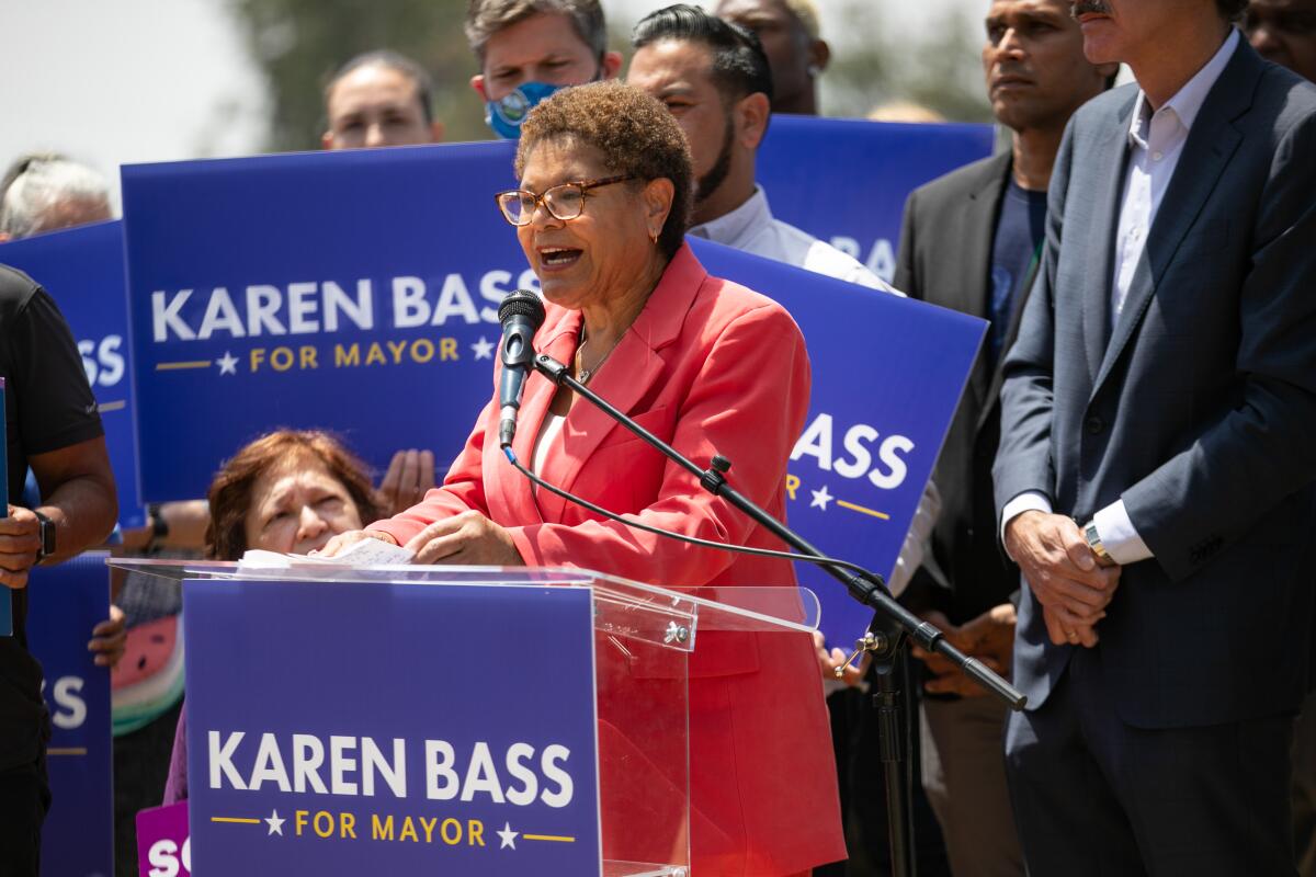 A woman at a podium speaking into a microphone. Signs say “Karen Bass for mayor.”
