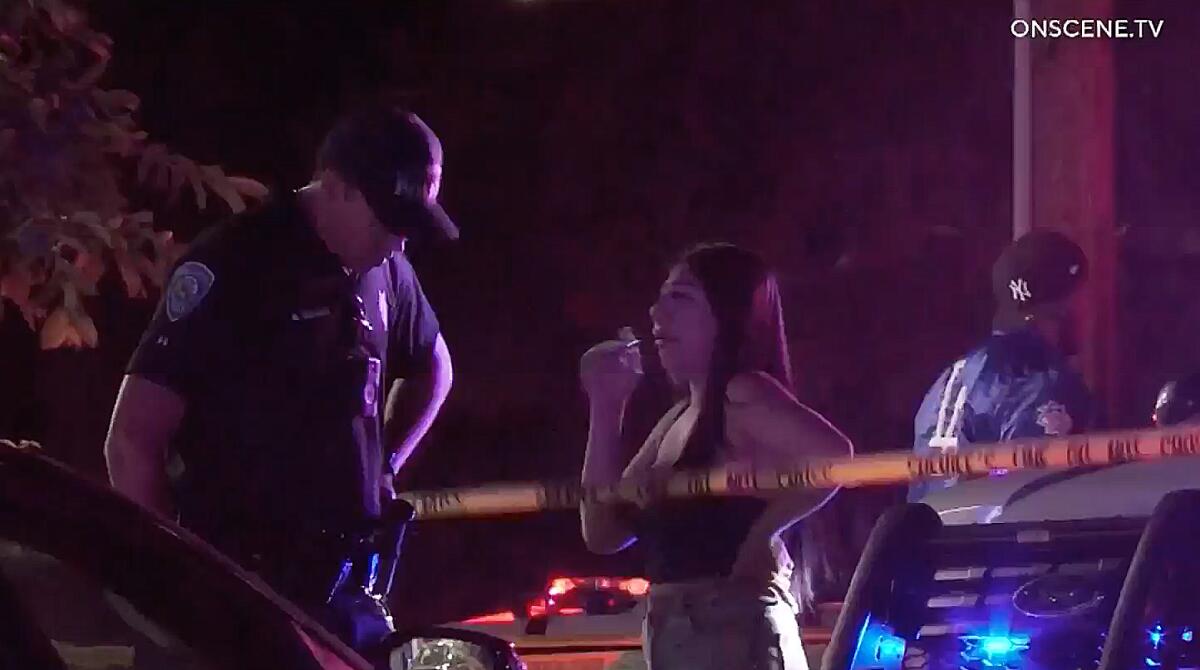 San Bernardino police officer talks to a woman near yellow police tape at night.