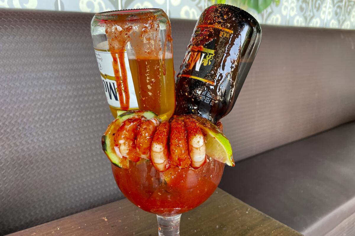 The Rubia y La Morena michelada is served in a glass goblet, with two beer bottles upside down in it plus shrimp.