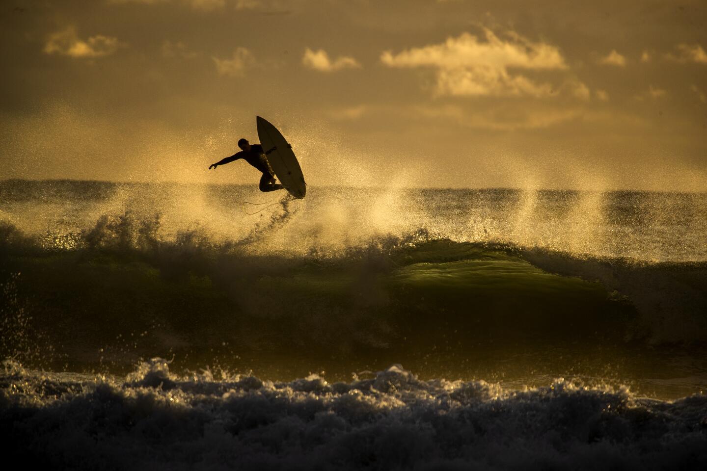 A surfer is silhouetted by the sunset as he is airborne off a big wave in between rain showers in Newport Beach, Calif., on Nov. 20, 2019.