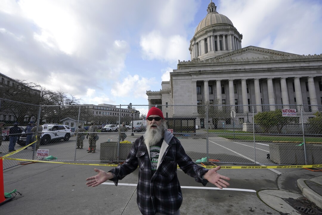 Rickie Day si trova al di fuori di una recinzione perimetrale al Campidoglio di Olympia, nello Stato di Washington. Membri della Guardia Nazionale e polizia stanno all'interno.