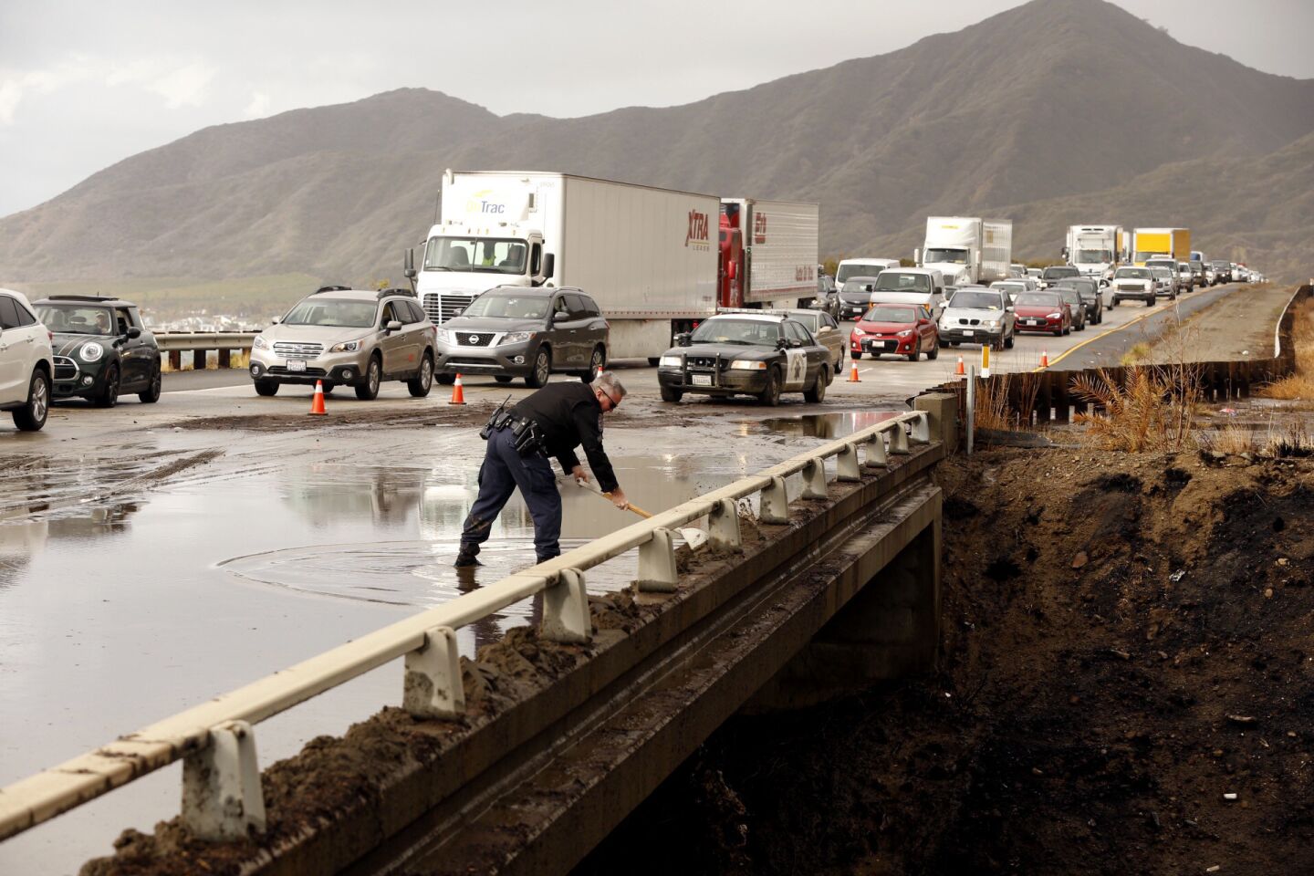 CHP Sgt. Joe Davy uses a shovel to try to clear a drain on the southbound lanes of the 101 Freeway of mud from the recent Solimar Fire runoff that flowed over the freeway, closing lanes.