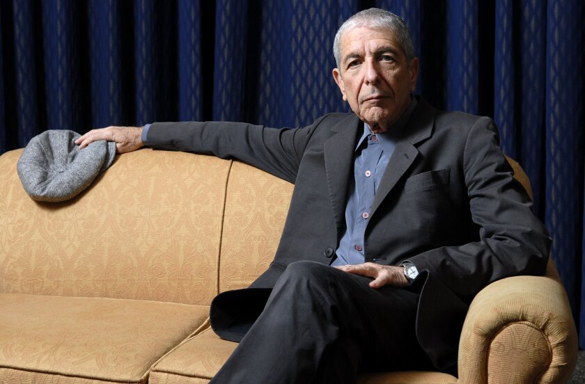 Leonard Cohen wears a suit while sitting on a couch and holding his hat