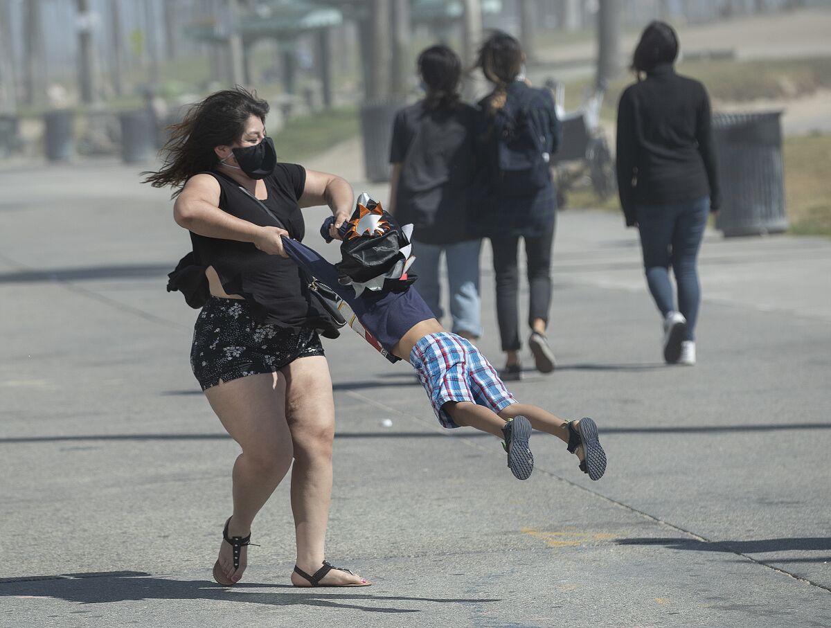 A masked Bell Vasquez, 28, of Los Angeles takes her son Israel, 4, for a spin while visiting the boardwalk in Venice Beach.