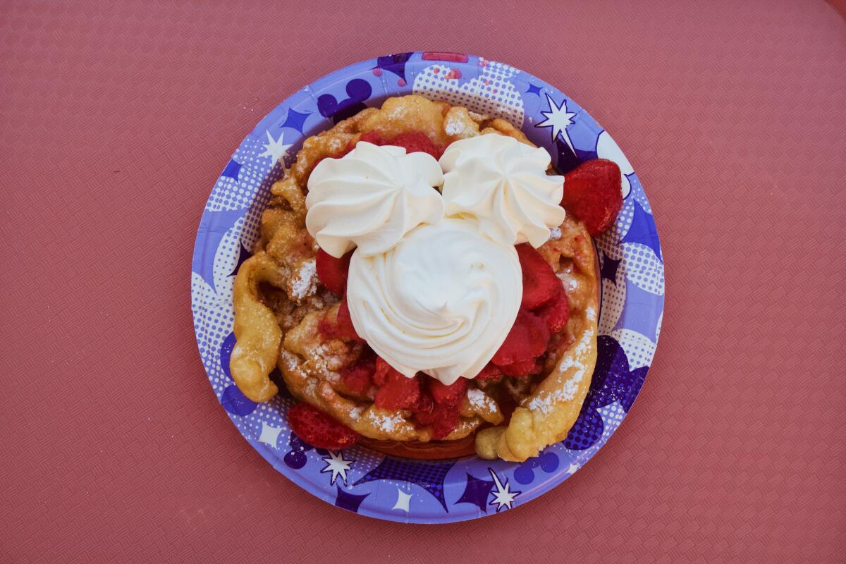 An overhead photo of a strawberry-topped funnel cake featuring whipped cream in the shape of Mickey Mouse