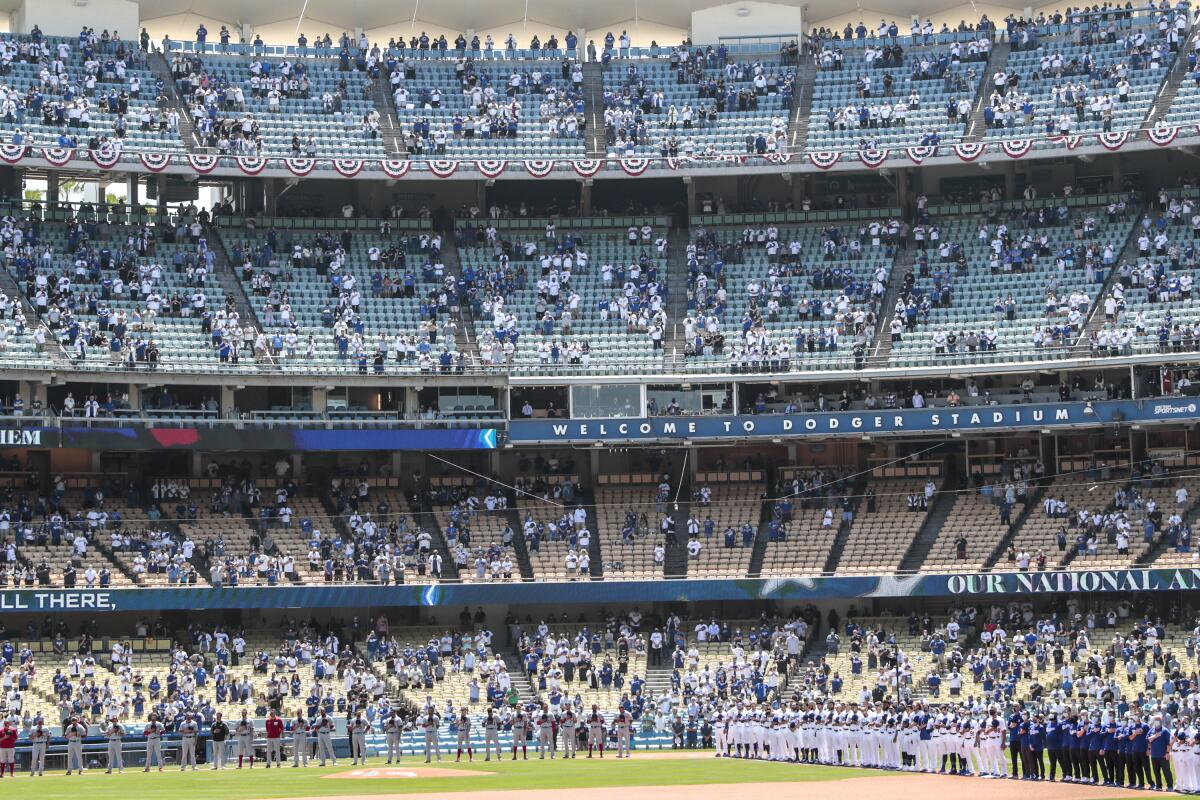 Dodgers and Nationals players line up on the field. Four decks of stadium seating, behind them, are half filled.