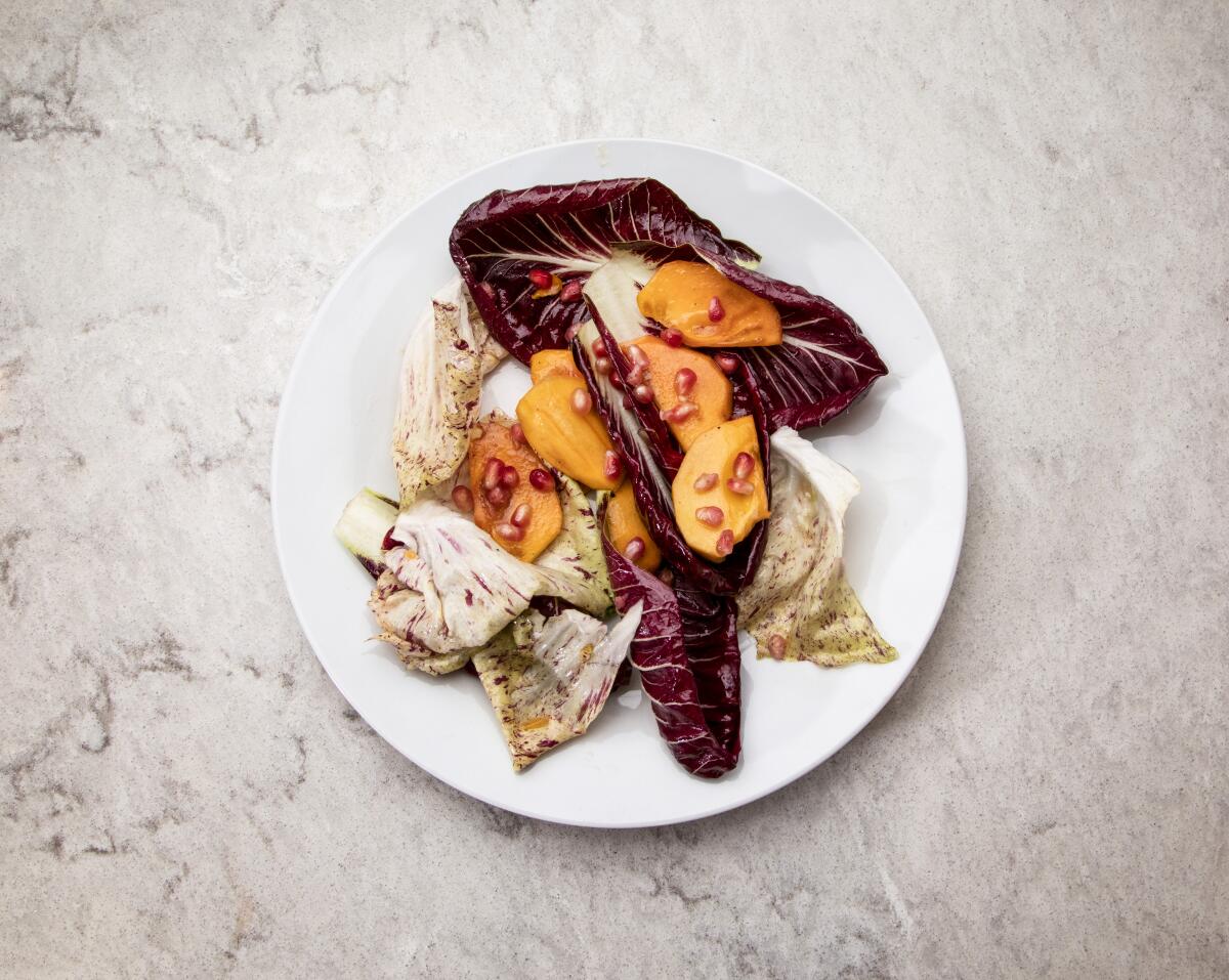 A white plate with a salad of red and white lettuce leaves, persimmon chunks and pomegranate seeds