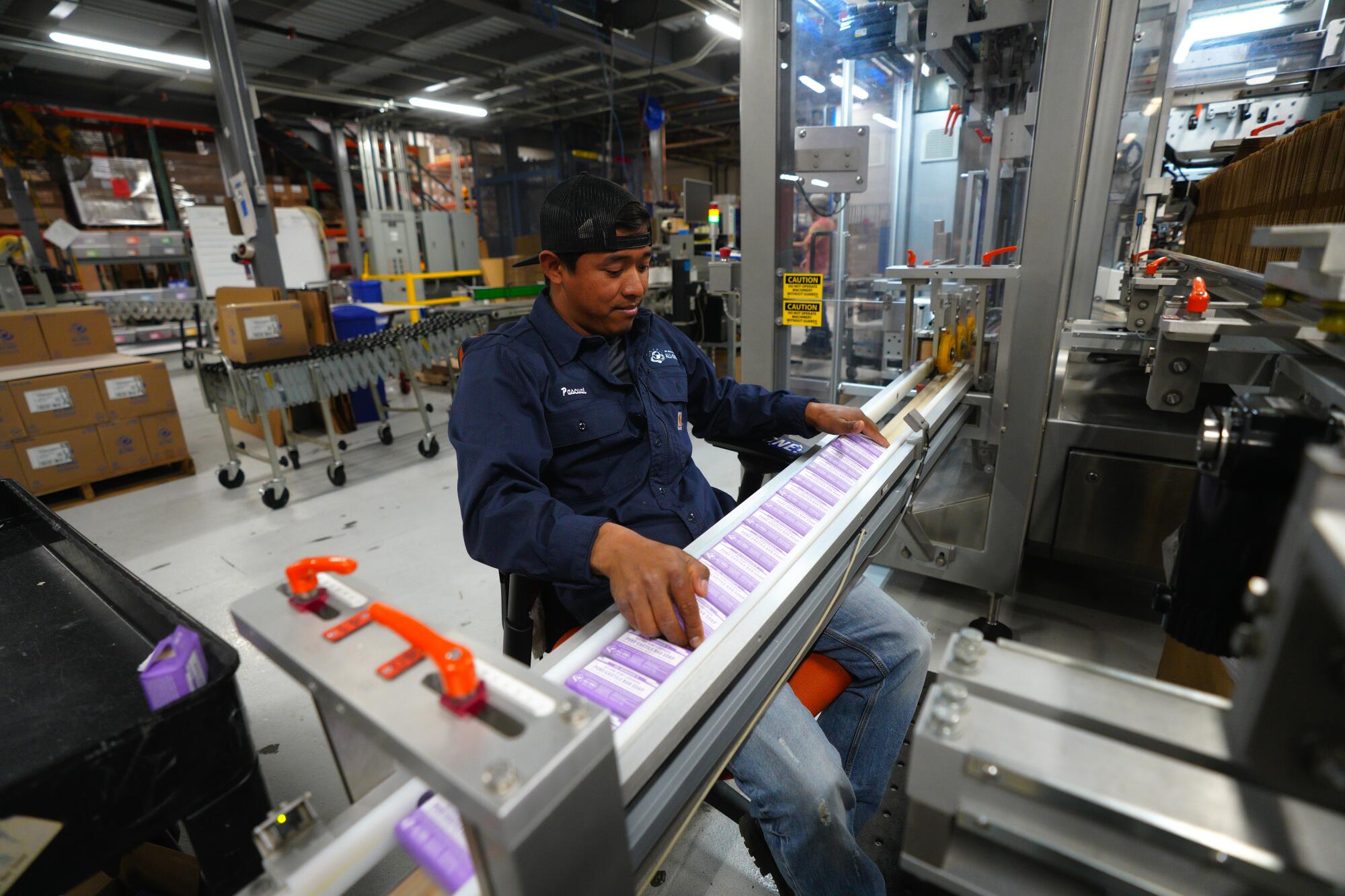 A man checking bars of soap with lavender labels as they come down a production line in a factory