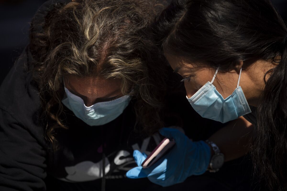 In the midst of the coronavirus pandemic, Dr. Susan Partovi, left, and nurse practitioner Jen King administer medical aid to a man in a Home Depot parking lot in Los Angeles.