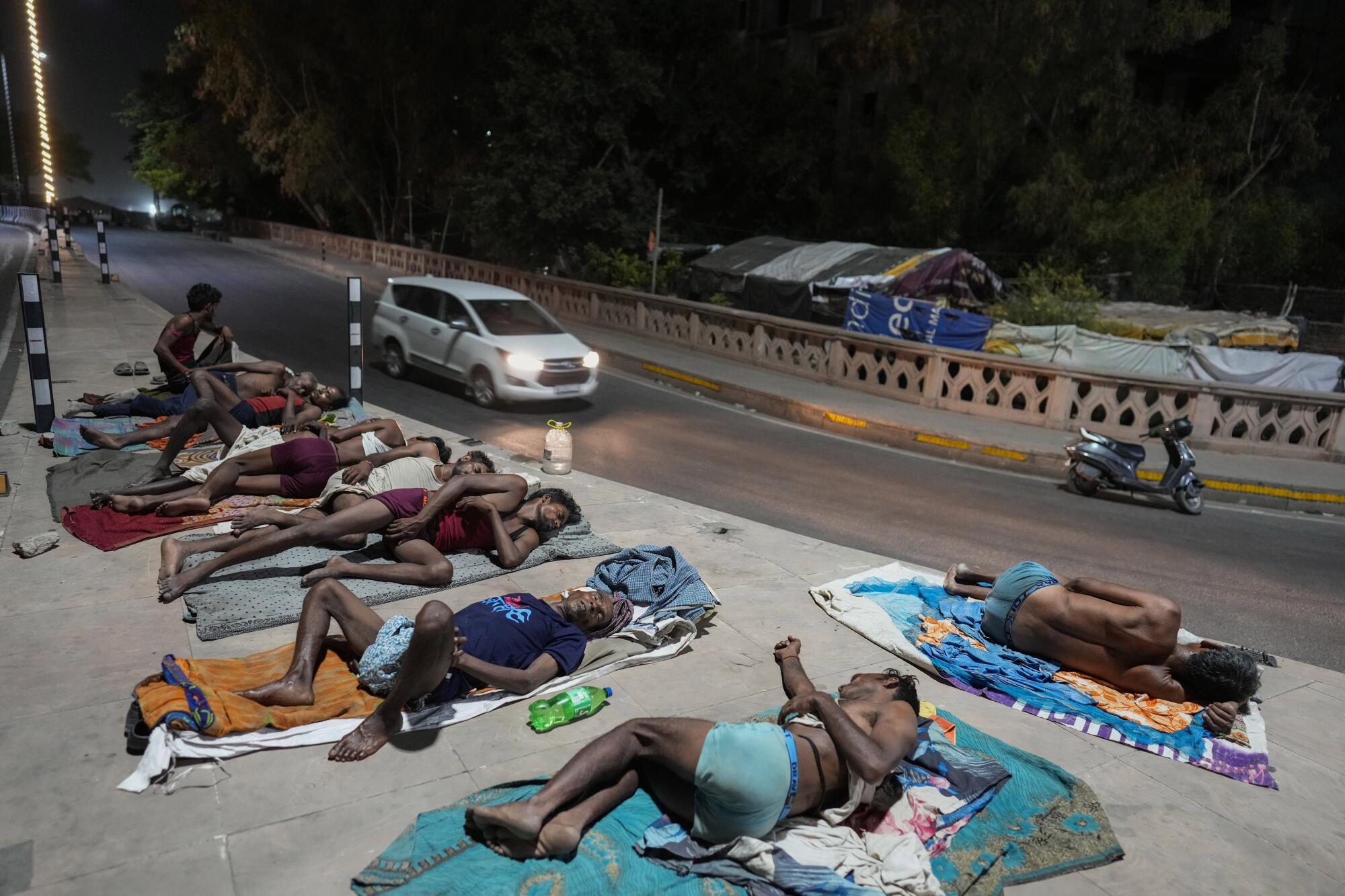 People sleeping on towels on a sidewalk as a white van drives by 