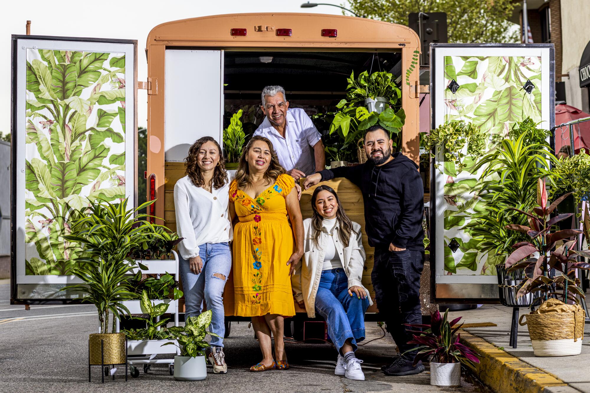 Three women and two men in a family stand in front of a pink plants truck 