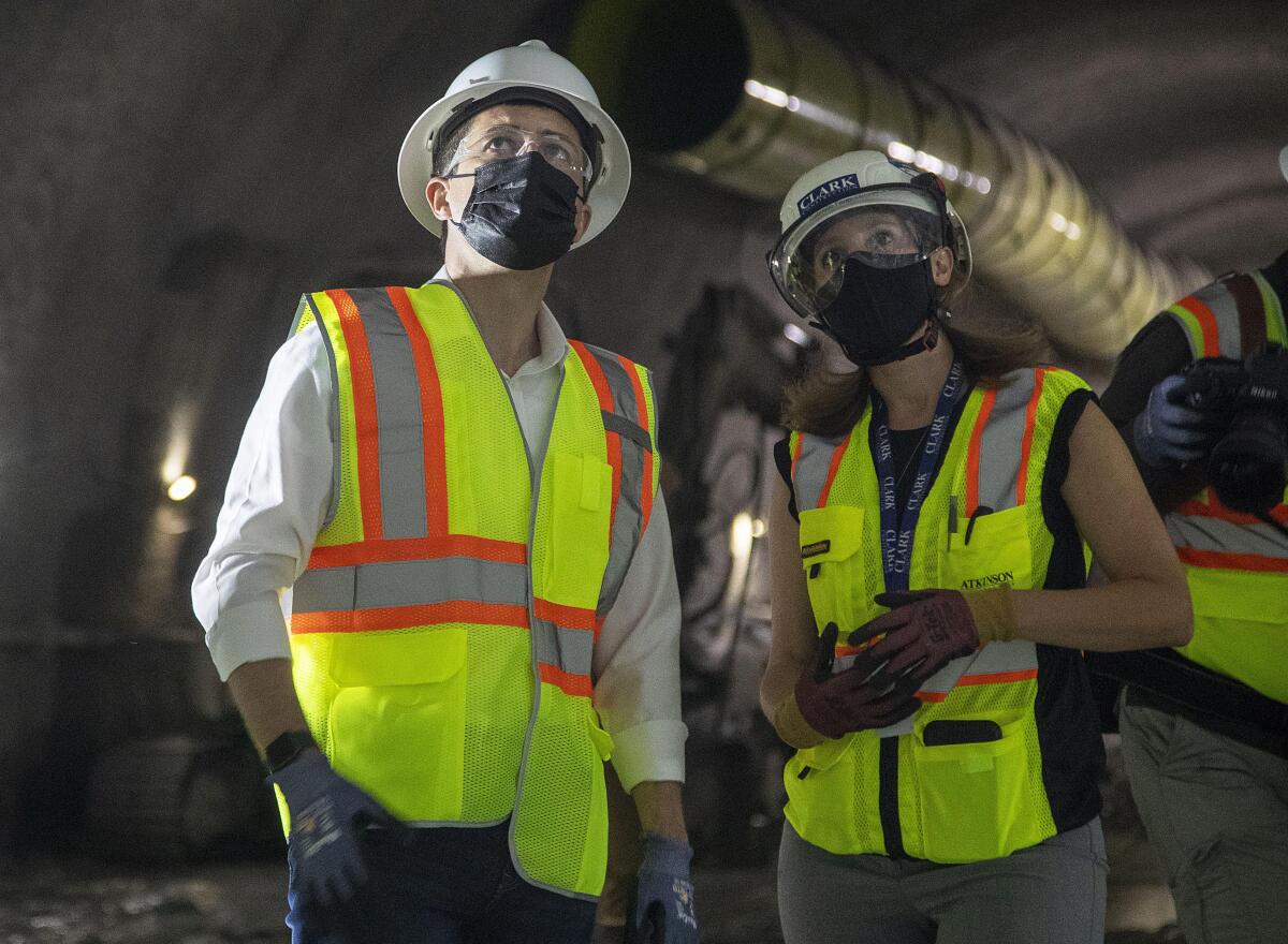 A man and a woman in yellow and orange safety vests and hard hats in an underground tunnel