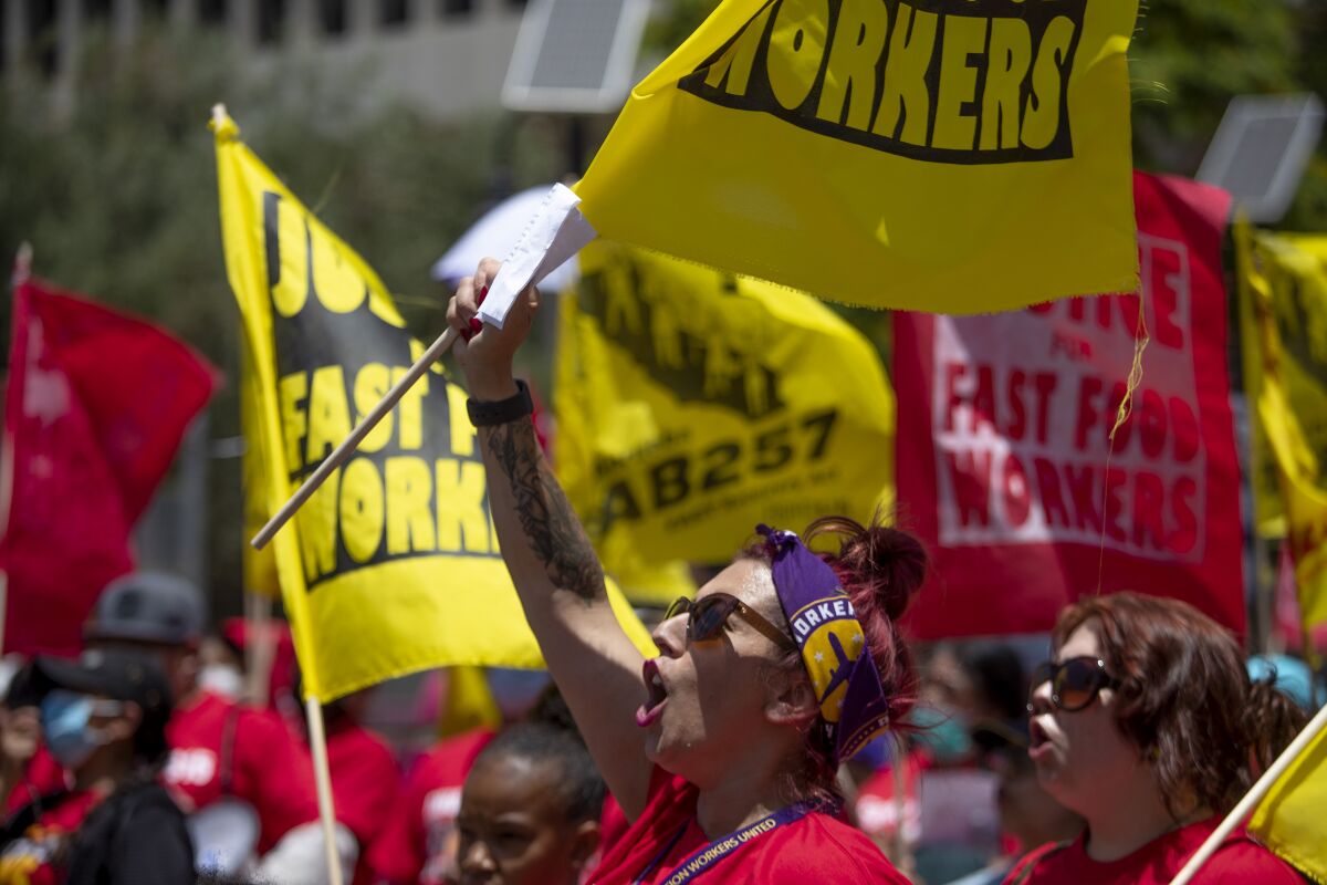 People waving flags and "Justice for Fast Food Workers" signs at a protest.