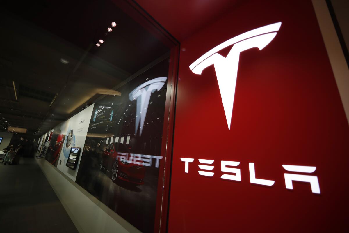 A red-and-white sign bearing the Tesla logo is displayed outside a Tesla store.