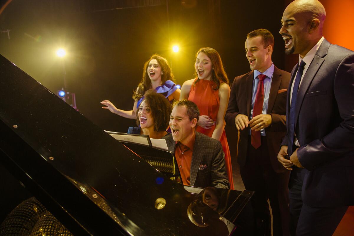 Lesli Margherita, Andrea Ross, Ryan Vona, Nicholas Christopher, Ashley Blanchet and Andy Einhorn sing around a piano.