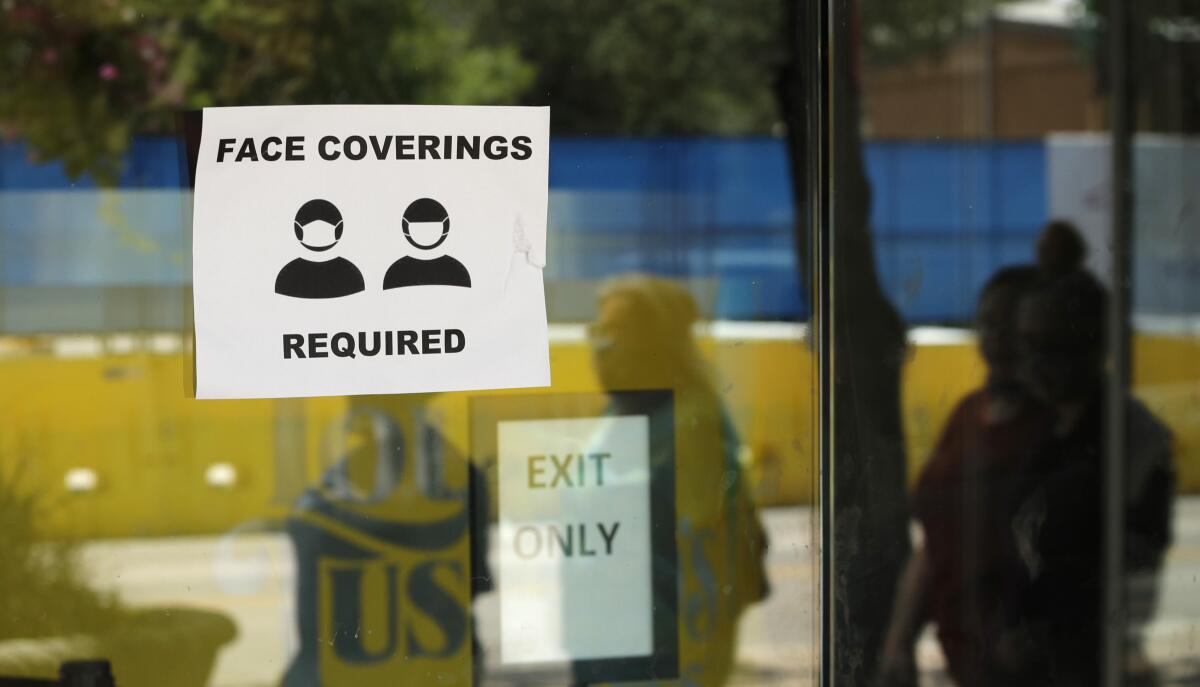 The images of passersby are reflected next to a sign requiring face coverings at a business in San Antonio, Texas.
