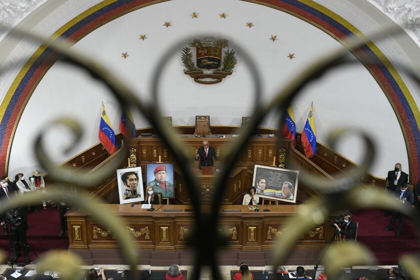 Seen through a balcony gate, the new president of Venezuela's National Assembly Jorge Rodriguez addresses newly sworn-in lawmakers as he is surrounded by photos of late Venezuelan President Hugo Chavez and independence hero Simon Bolivar at Congress in Caracas, Venezuela, Tuesday, Jan. 5, 2021. The ruling socialist party assumed the leadership of Venezuela's congress on Tuesday, the last institution in the country it didn't already control. (AP Photo/Matias Delacroix)