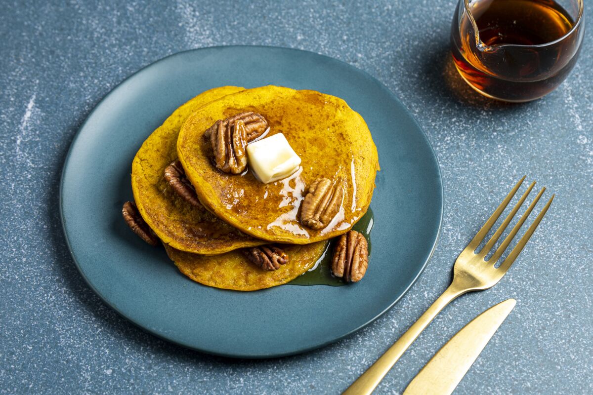 Vegan pumpkin pancakes topped with pecans, butter and syrup.
