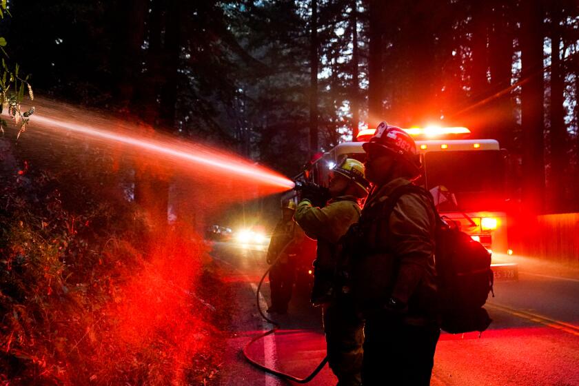 Firefighters tackle hotspots along Highway 9 during the CZU Lightning Complex fire Sunday in Boulder Creek, Calif.